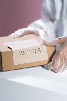 Gloved hands holding a labeled vaccine box in a clinical setting.